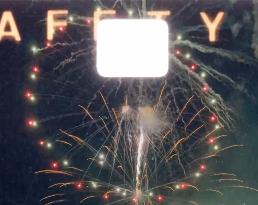 VSCO 8mm film frame overlaid on a video still of fireworks exploding at night in front of partially visible letters spelling 'SAFETY'.