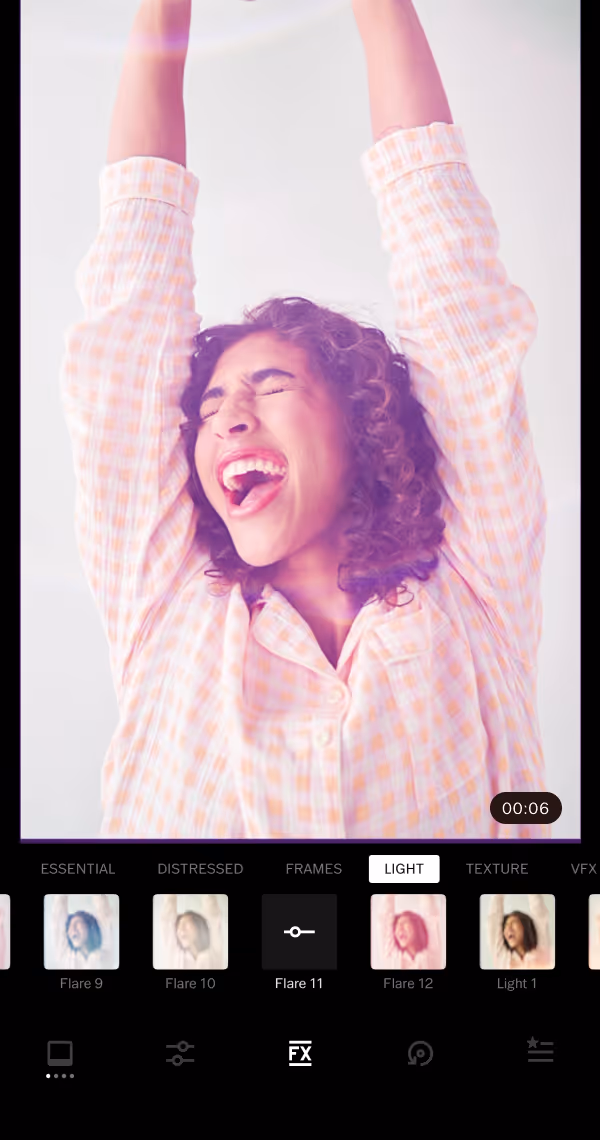 Video light effects menu with Lens Flare 11 selected in the VFX section of the VSCO mobile app on a video still of a woman with curly hair wearing a checkered shirt raising her arms and smiling joyfully with her eyes closed.