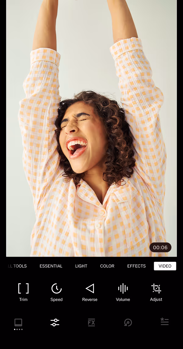 Video editing tools menu in the VSCO mobile app on a video still of a woman with curly hair wearing a checkered shirt raising her arms and smiling joyfully with her eyes closed.