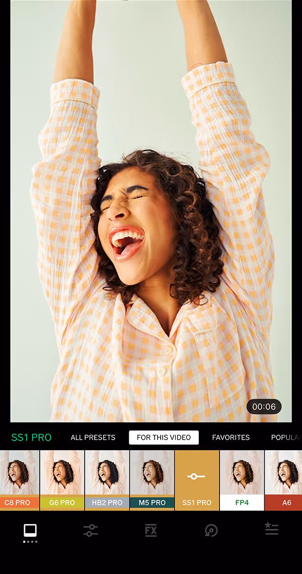 Video filter menu in VSCO app with 'For This Video' and 'SS1' selected showing a video still of a woman with curly hair wearing a checkered shirt raising her arms and smiling joyfully with her eyes closed.