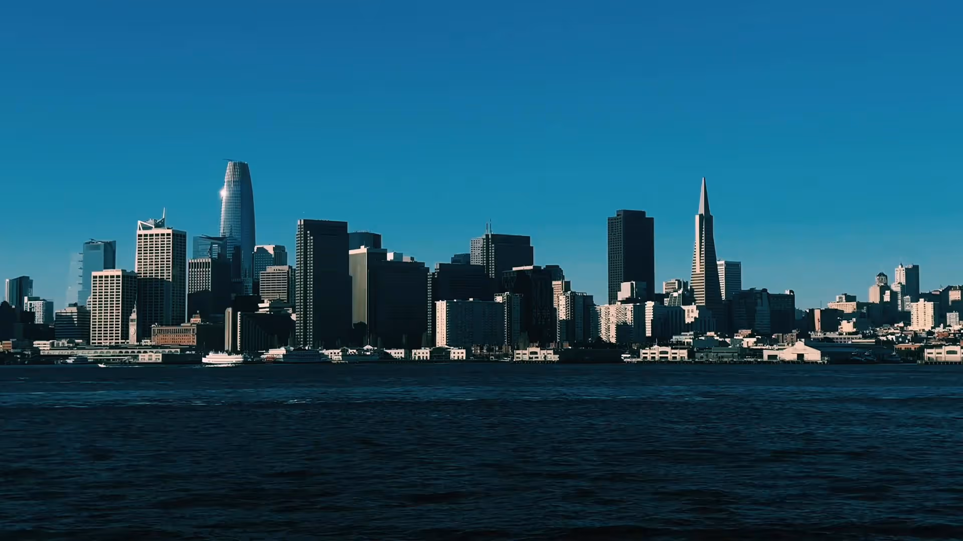 VSCO video filter applied to San Francisco skyline with prominent Salesforce Tower and Transamerica Pyramid against a clear blue sky, viewed across the water.