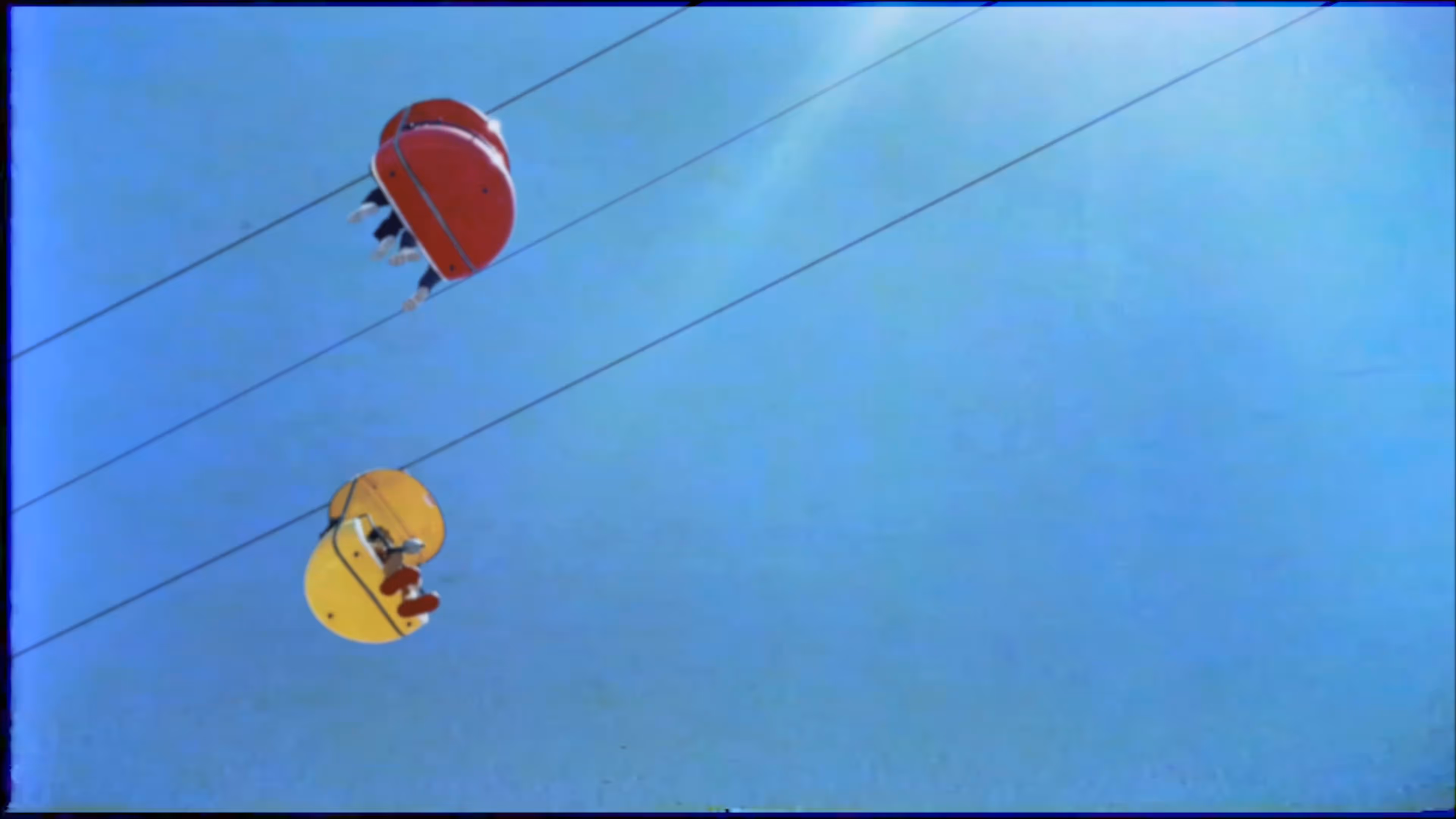 VHS filter on two colorful gondola cable cars suspended on wires against a clear blue sky.