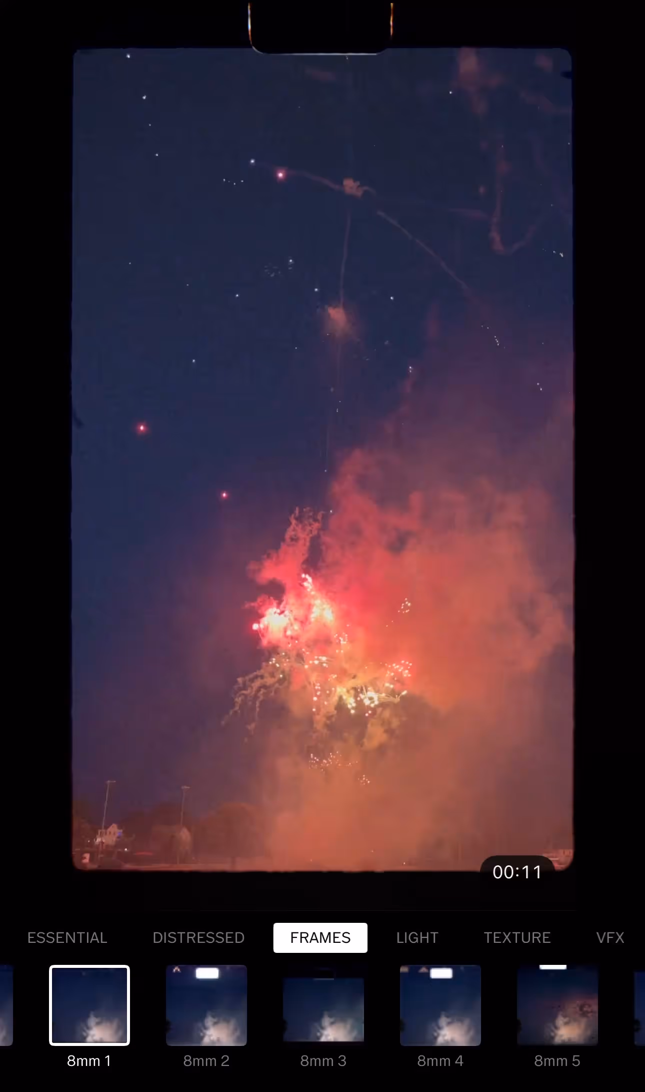 Fireworks exploding with red and yellow colors against a dark night sky, viewed through a phone screen with VSCO video editing app UI.