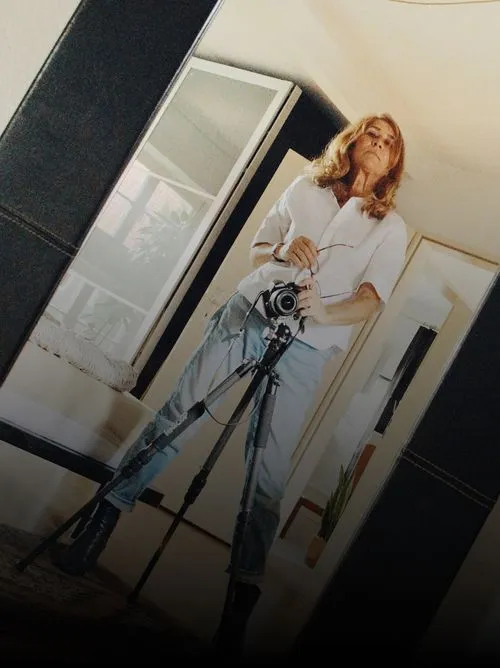 Photographer Luisa Aguiar taking a photo of herself in a full-length mirror using a camera on a tripod.