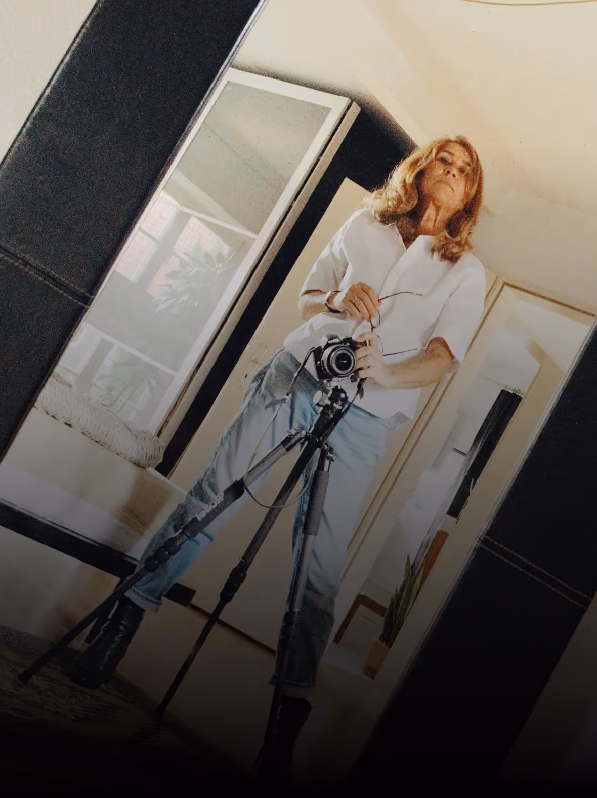 Photographer Luisa Aguiar taking a photo of herself in a full-length mirror using a camera on a tripod.