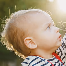 Batch edited family photoshoot of a side profile of a toddler with blonde hair looking upward in soft outdoor sunlight.