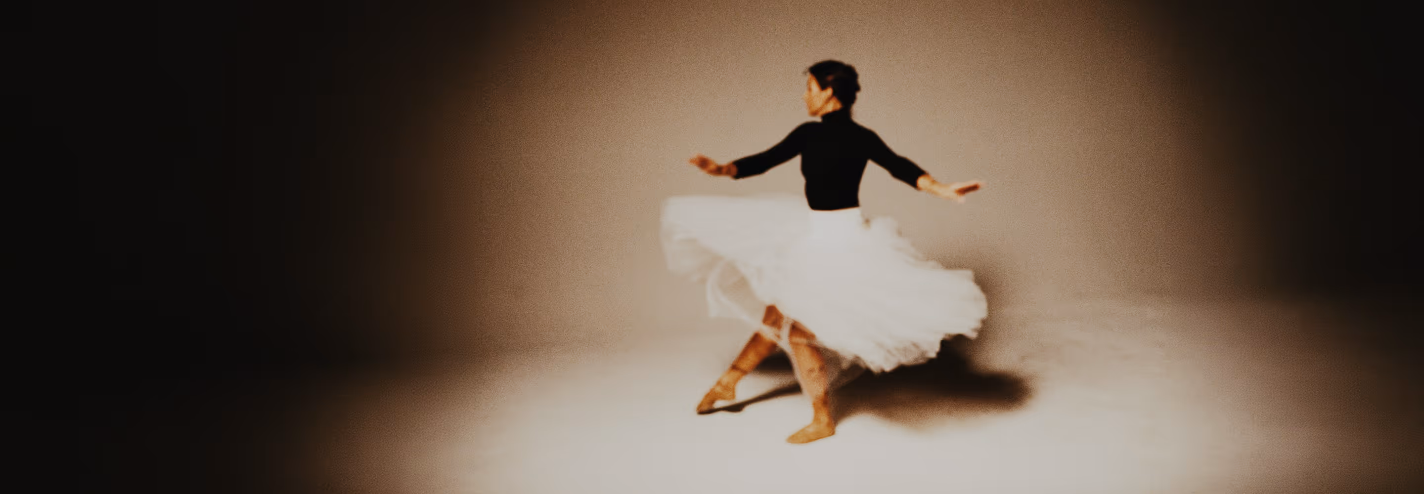 Image edited in Studio Pro of a ballerina spinning in a white tutu and black top on a softly lit stage with a shadow on the floor.
