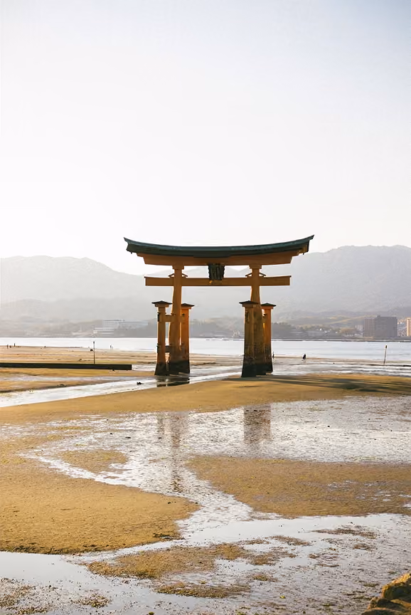 Large traditional Japanese torii gate standing in shallow water with mountains in the background at low tide with crowd of people removed using AI