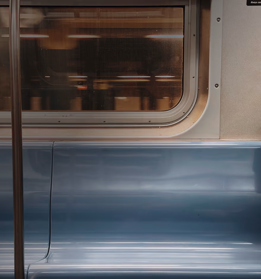 Empty blue plastic seats and a window inside a subway train car with a metal pole to the left.