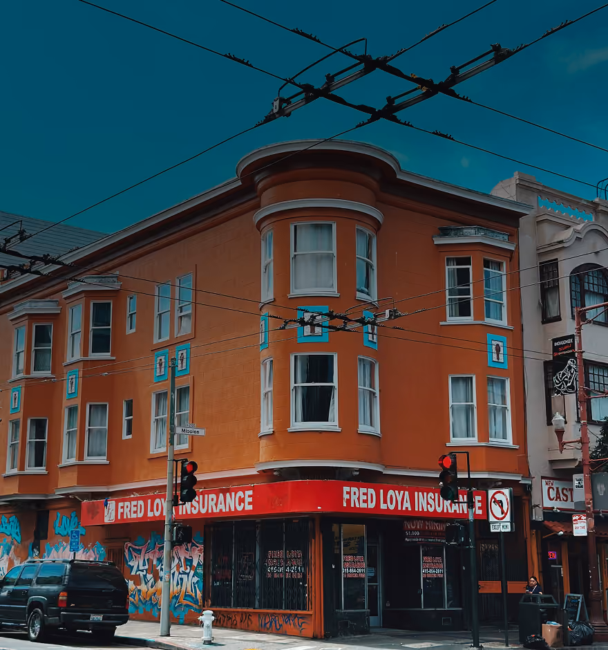 Orange corner building with red signs and graffiti on lower walls at street intersection.
