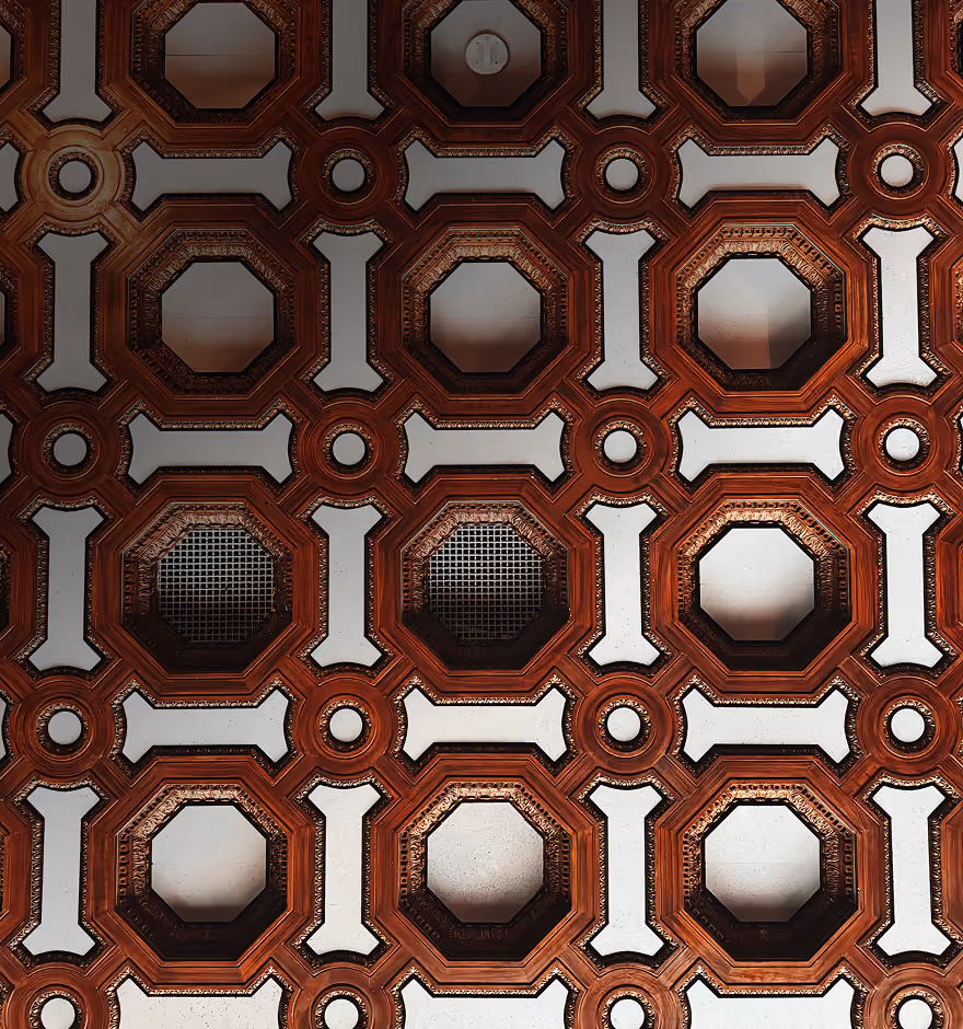 Decorative ceiling with repeating octagonal wooden frames and white panels, some with mesh inserts.