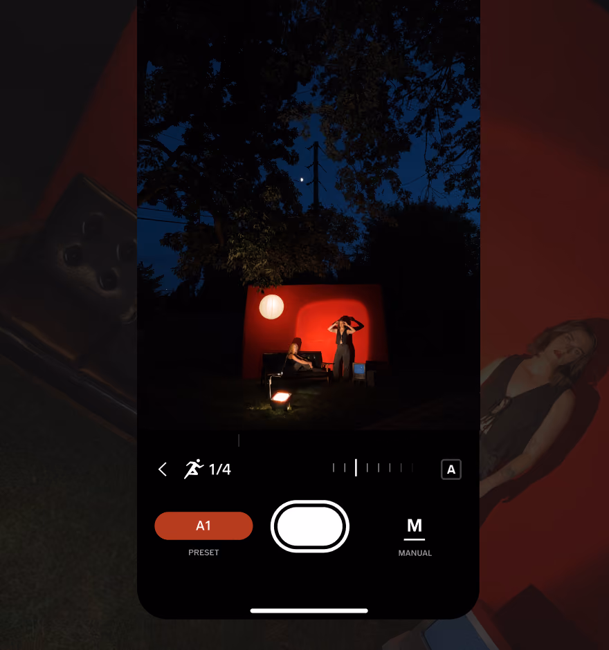 Mobile phone screen camera app showing a night photo of two people by a red wall with a round light and trees.