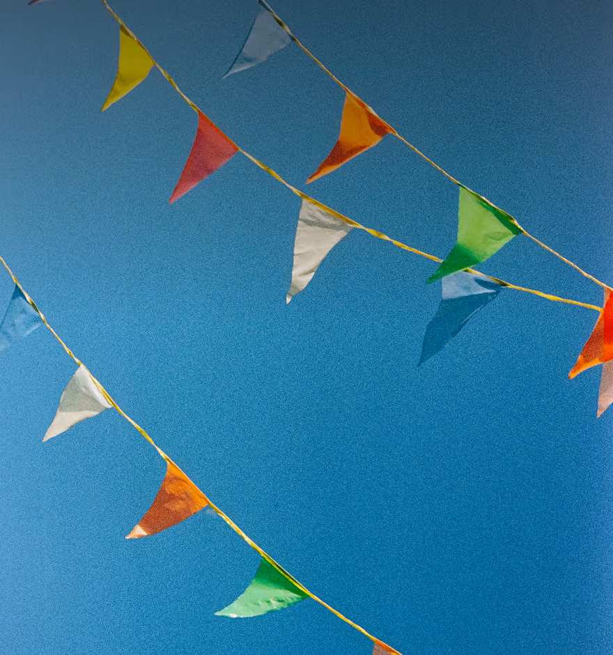 Colorful triangular pennant flags strung diagonally against a blue sky background.
