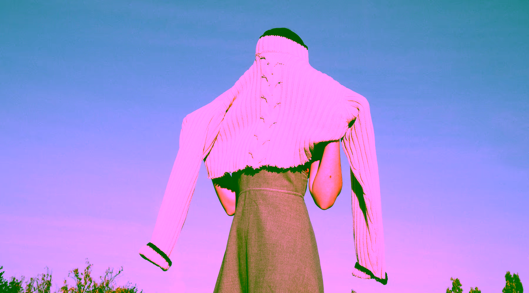 Person wearing a cream knit sweater over their head with arms extended against a clear blue sky.
