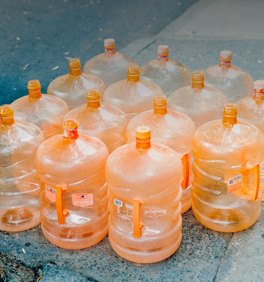 Group of large empty orange water jugs arranged on a concrete ground outdoors.
