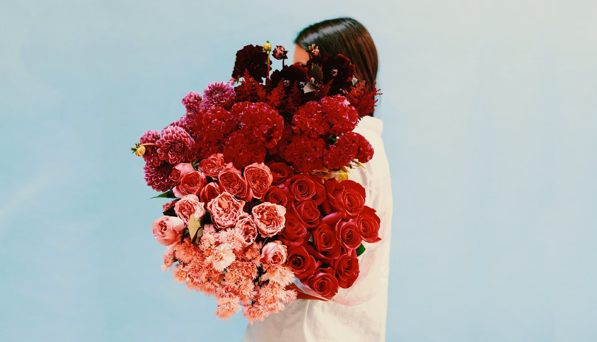 Film filter added to an image of a person in white shirt holding a large bouquet of red and pink flowers against a plain light blue background.