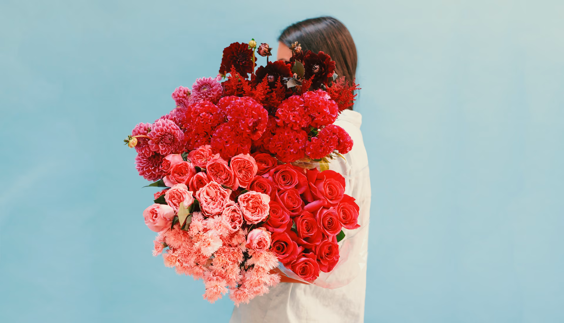Original unedited image of a person in white shirt holding a large bouquet of red and pink flowers against a plain light blue background.
