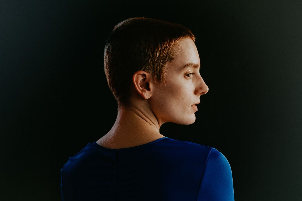 Portrait of a person in a blue top looking over their shoulder in profile against a dark background, original unedited