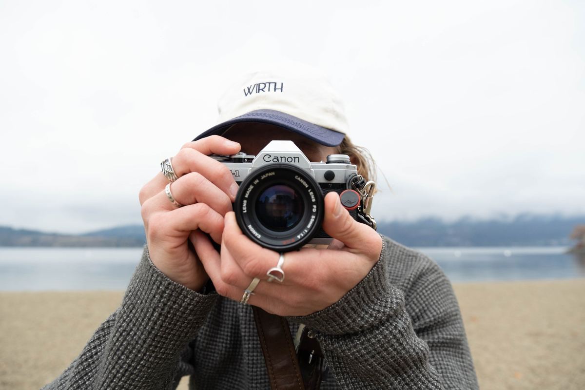 Photographer holding a film camera up to their face on a lakeshore, original unedited