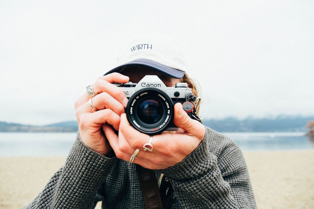 Photographer holding a film camera up to their face on a lakeshore, Agfa Vista 400 preset applied