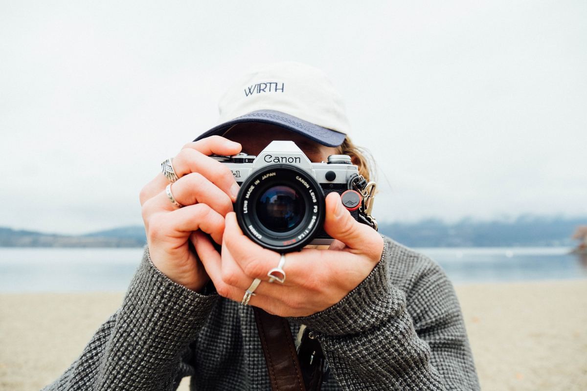 Photographer holding a film camera up to their face on a lakeshore, Kodak Gold 100 preset applied