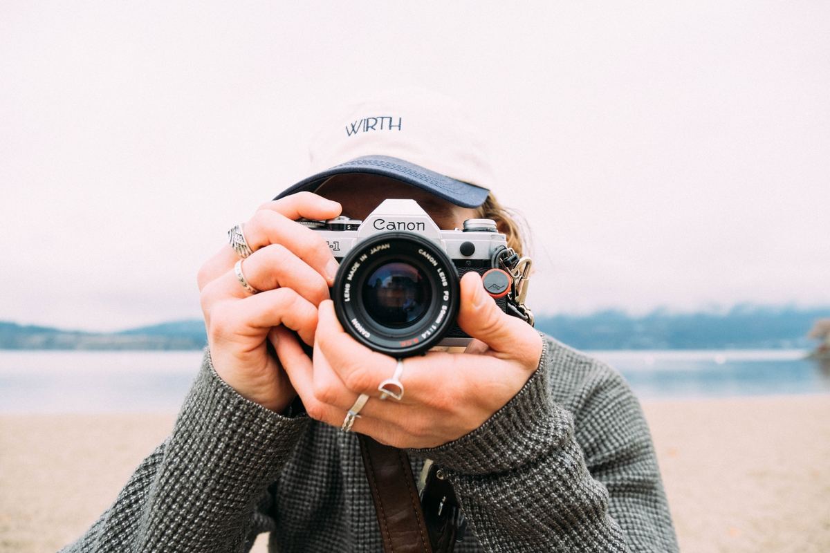 Photographer holding a film camera up to their face on a lakeshore, Agfa Vista 100 preset applied