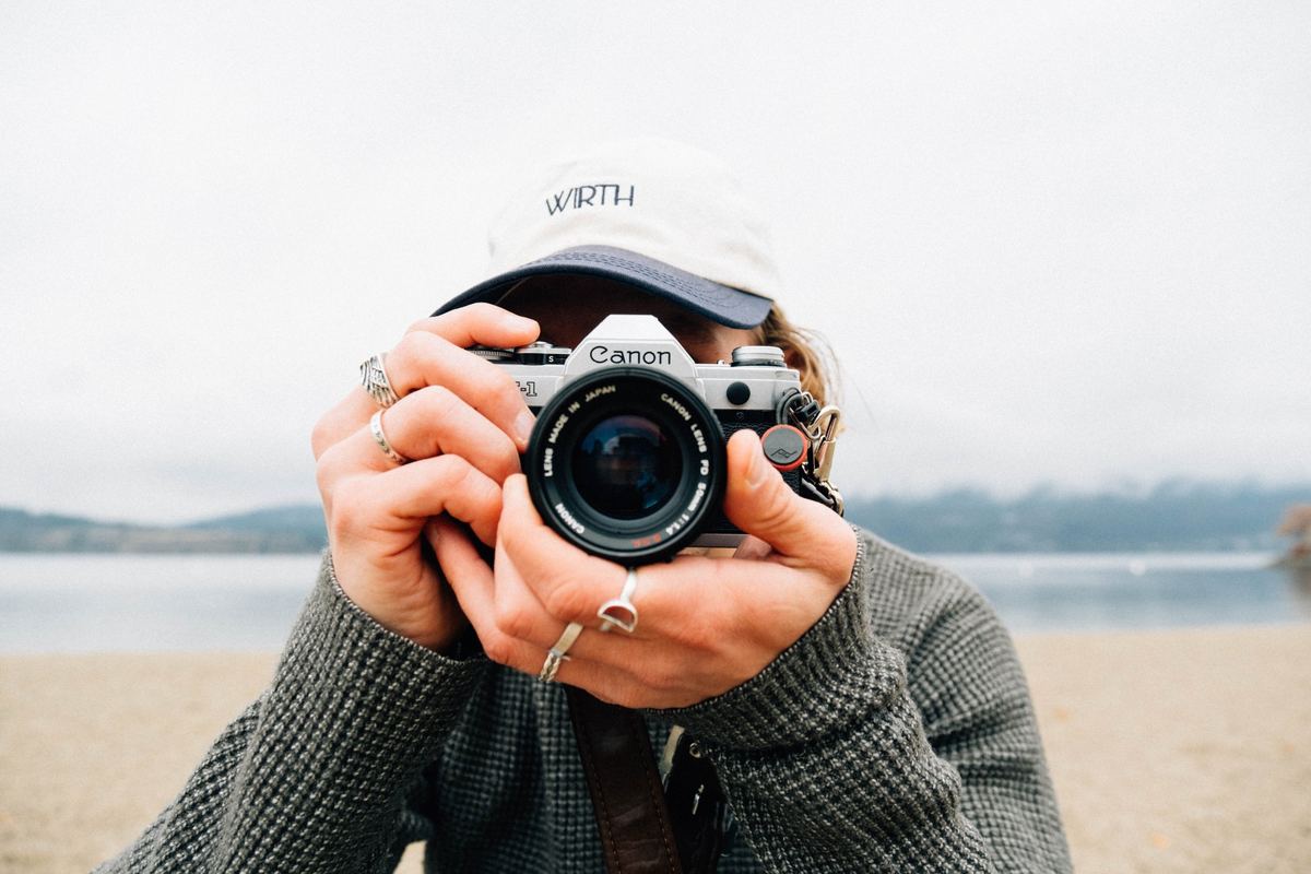Photographer holding a film camera up to their face on a lakeshore, Kodak Gold 200 preset applied