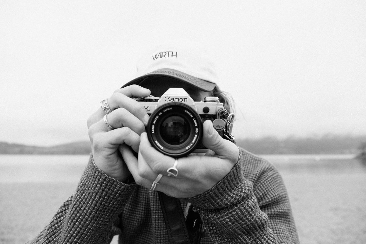 Photographer holding a film camera up to their face on a lakeshore, Kodak BW400CN preset applied