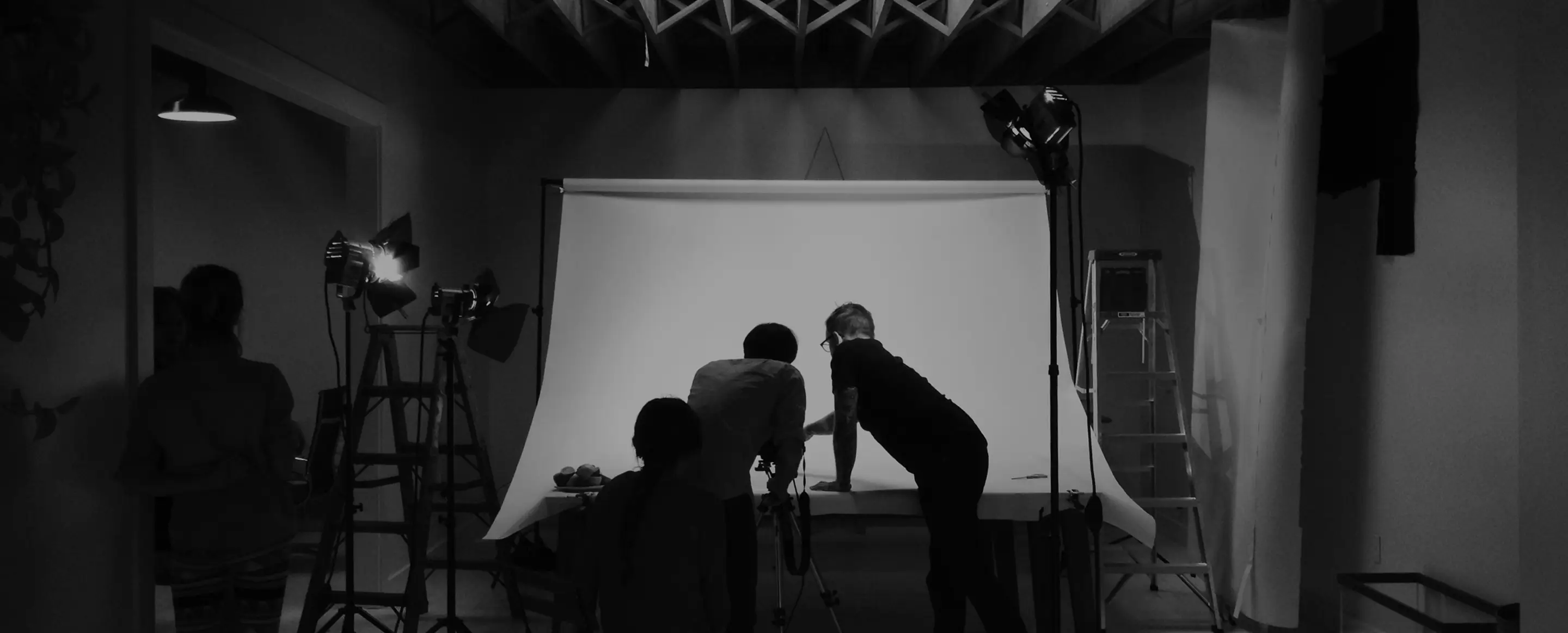 Black and white photo of a photo crew working in front of a white seamless backdrop with studio lights.