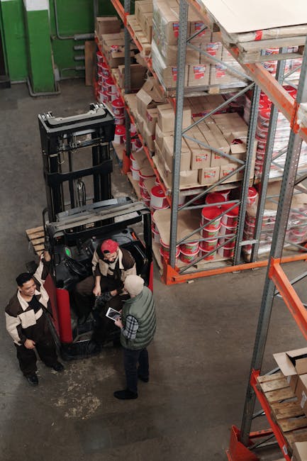 High-angle view of warehouse employees operating a forklift surrounded by stacked shelves.