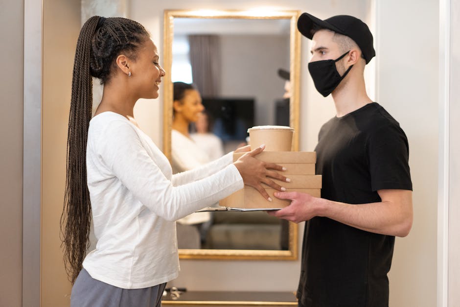 A delivery driver hands packages to a smiling woman indoors, showcasing modern online shopping convenience.