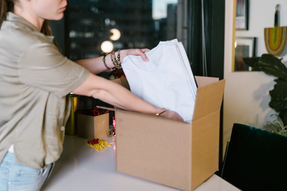 A woman packs white t-shirts into a cardboard box, set in a modern indoor environment.