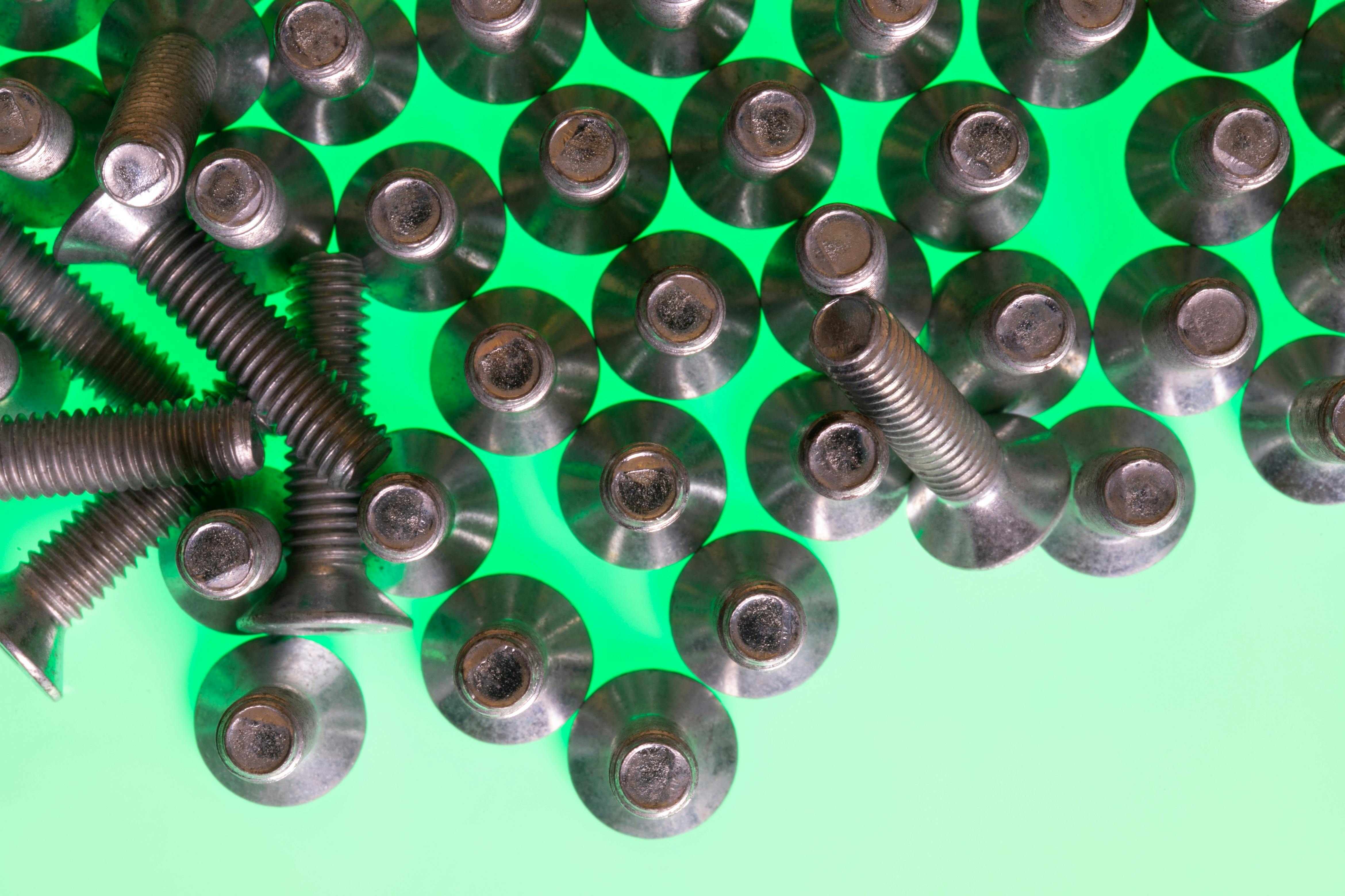 Close-up of metallic screws on a vibrant green surface, symbolizing technology and industry.