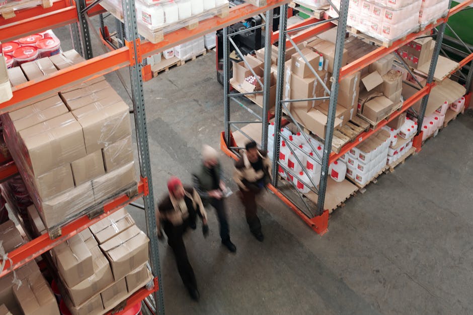 A high angle view of workers in motion in a busy warehouse with shelves full of boxes and packages.