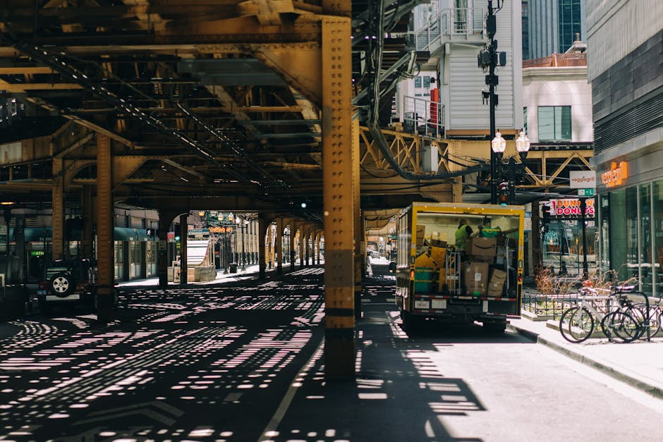 A busy Chicago street under elevated tracks with a delivery truck and bicycles, showcasing urban life.