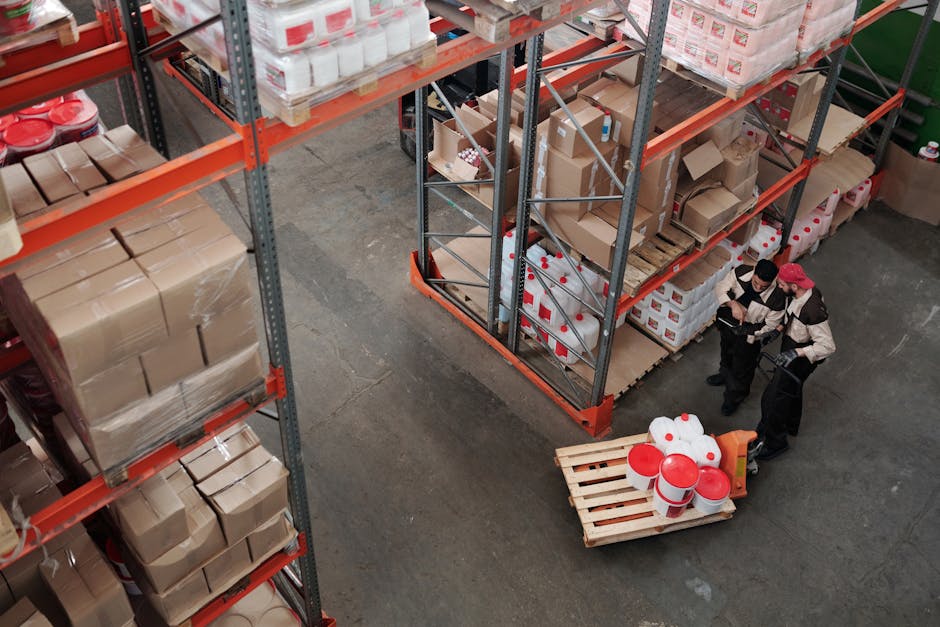 Workers managing inventory on shelves in a warehouse, viewed from above.