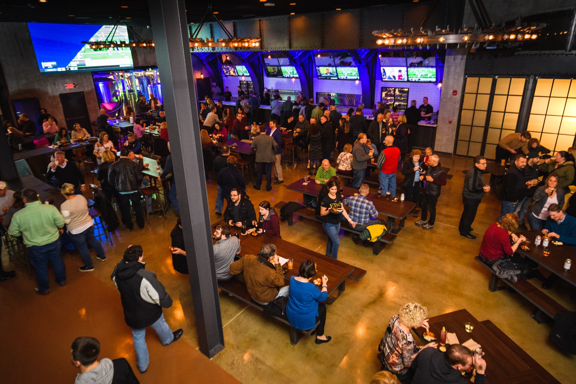 Large Elicit Brewing hall filled with people drinking, eating, and socializing at long wooden tables.