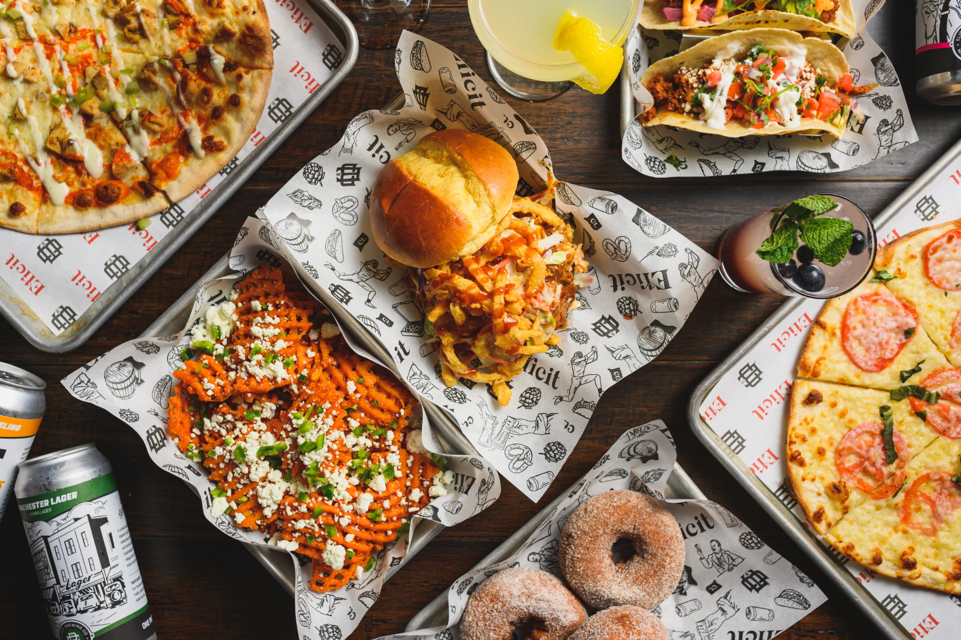 Food menu at Elicit Brewing featuring burgers, tacos, pizzas, and other dishes served with craft drinks on branded paper trays.