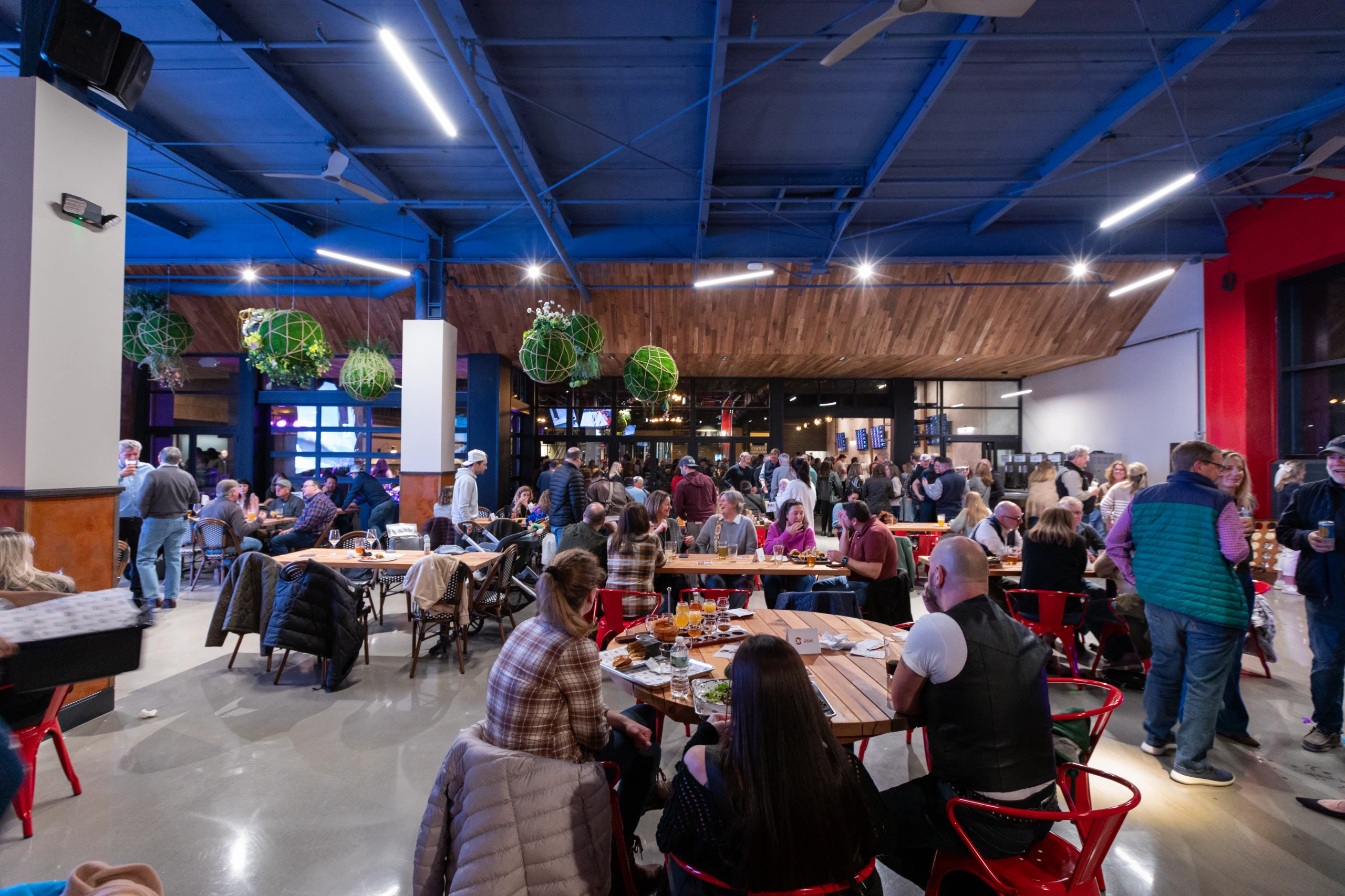 An image of a crowded beer hall at Elicit Brewing with guests sharing long tables, enjoying food and beer.