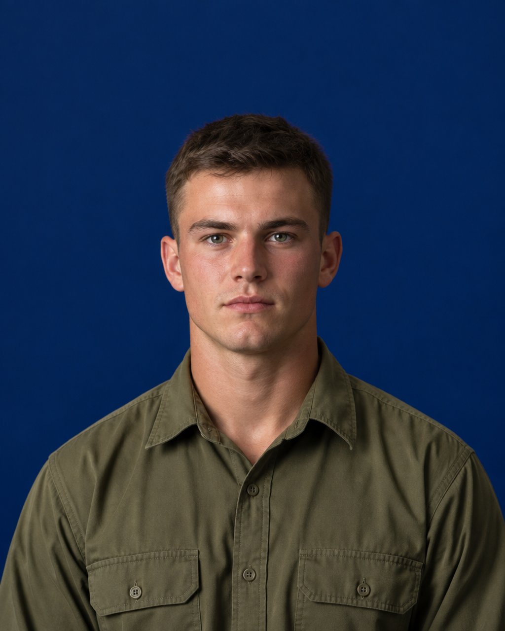 A young recruit in a plain olive field shirt against a deep navy studio backdrop