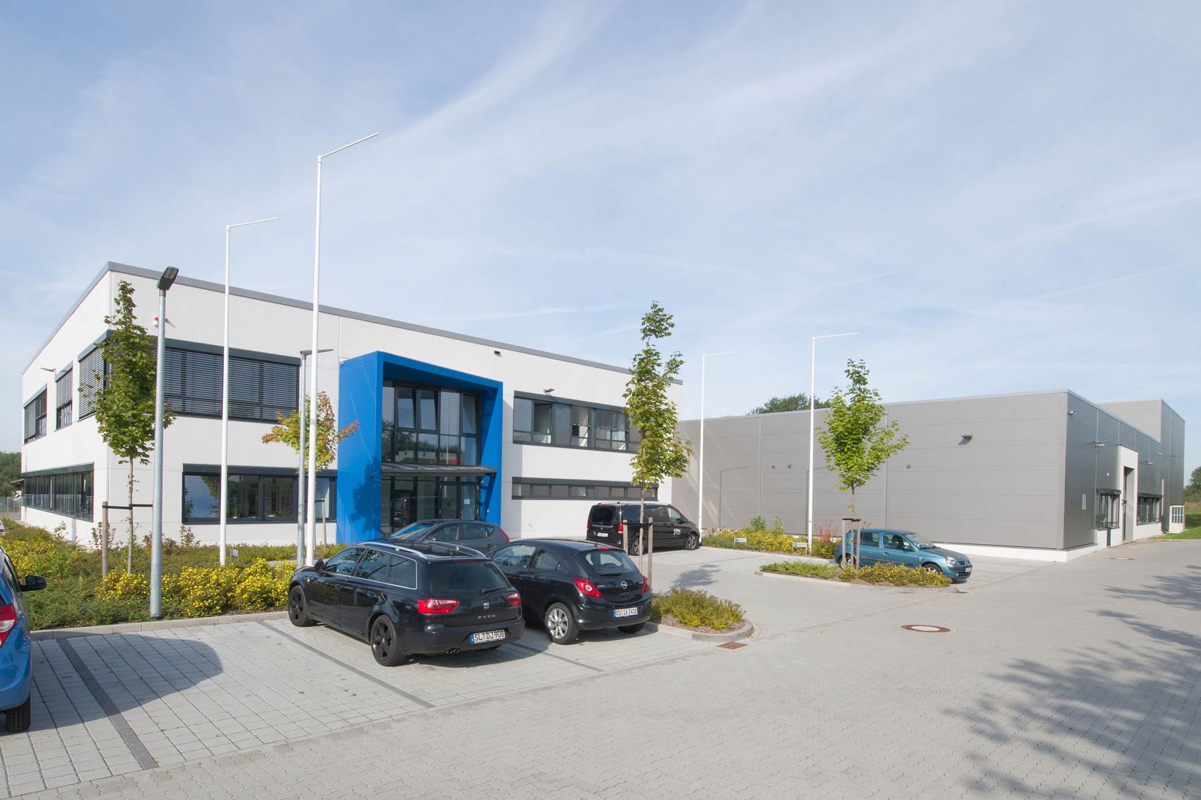 Werkhalle und Büro eines Maschinenbau-Unternehmens mit Zaun und geparktem Auto im Vordergrund.