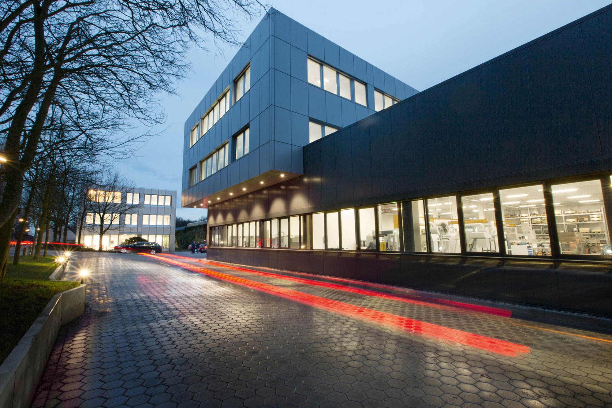 Werkhalle und Büro eines Maschinenbau-Unternehmens mit Zaun und geparktem Auto im Vordergrund.