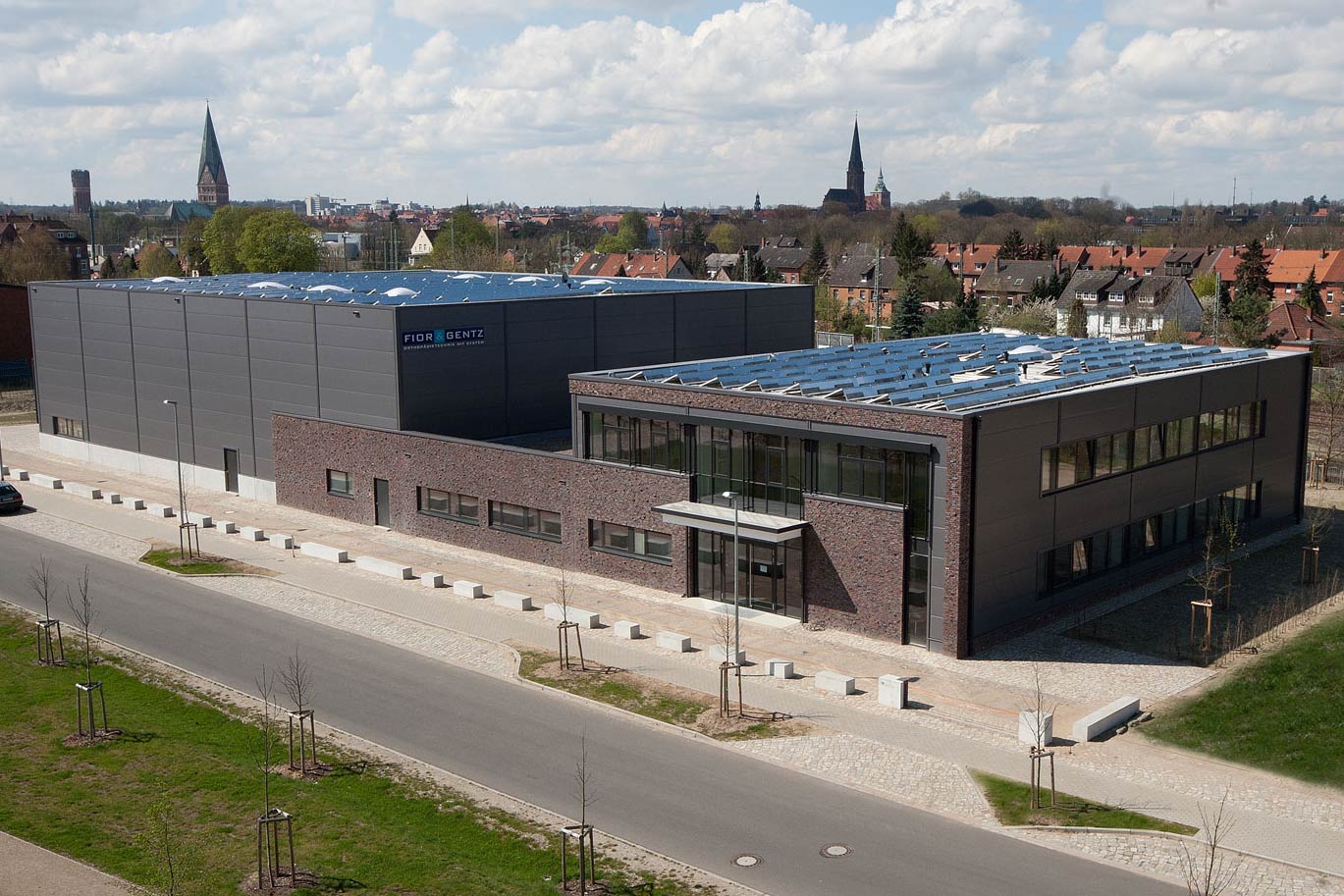 Werkhalle und Büro eines Maschinenbau-Unternehmens mit Zaun und geparktem Auto im Vordergrund.
