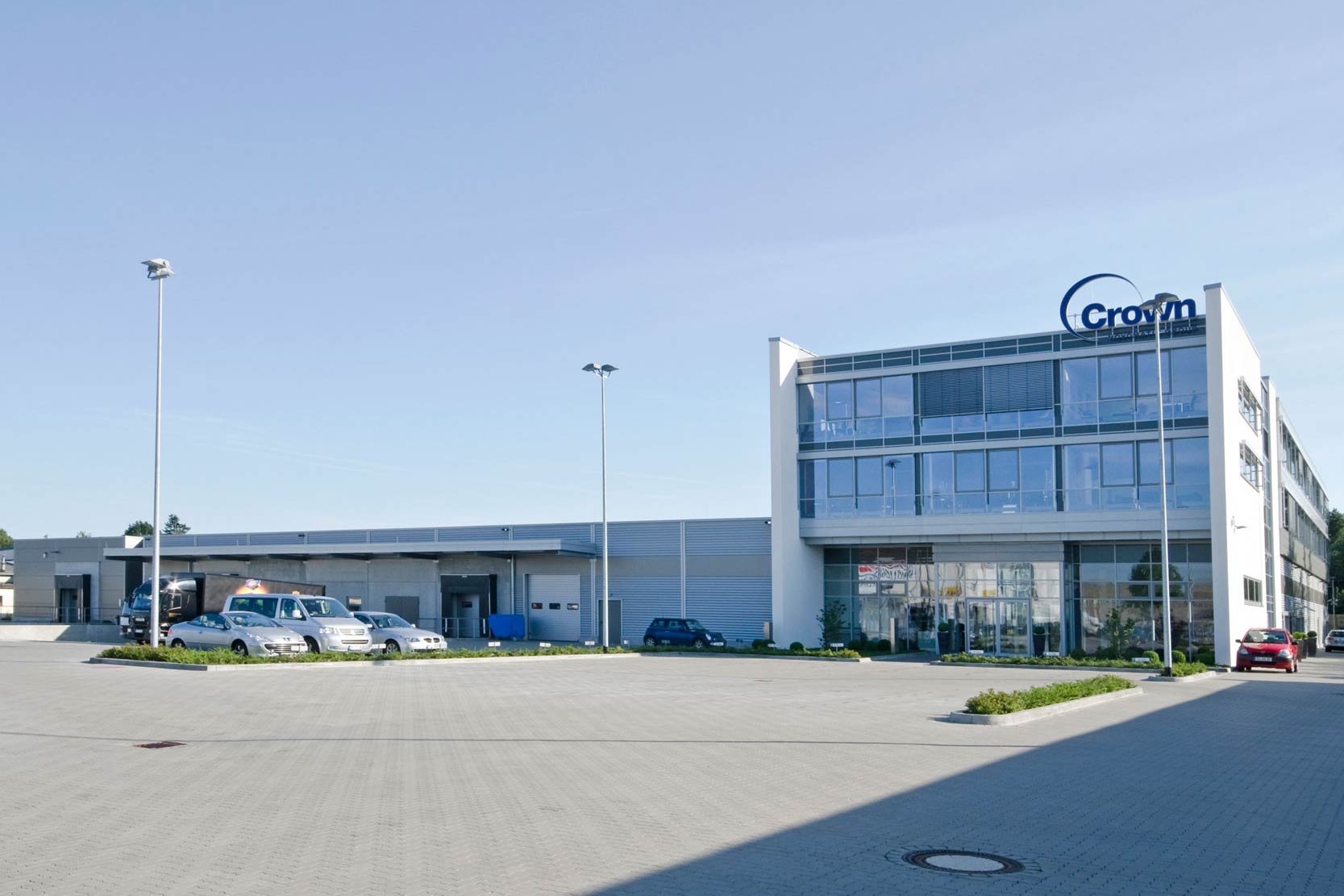 Graues Gebäude im Hintergrund, im Vordergrund ein Parkplatz mit Autos