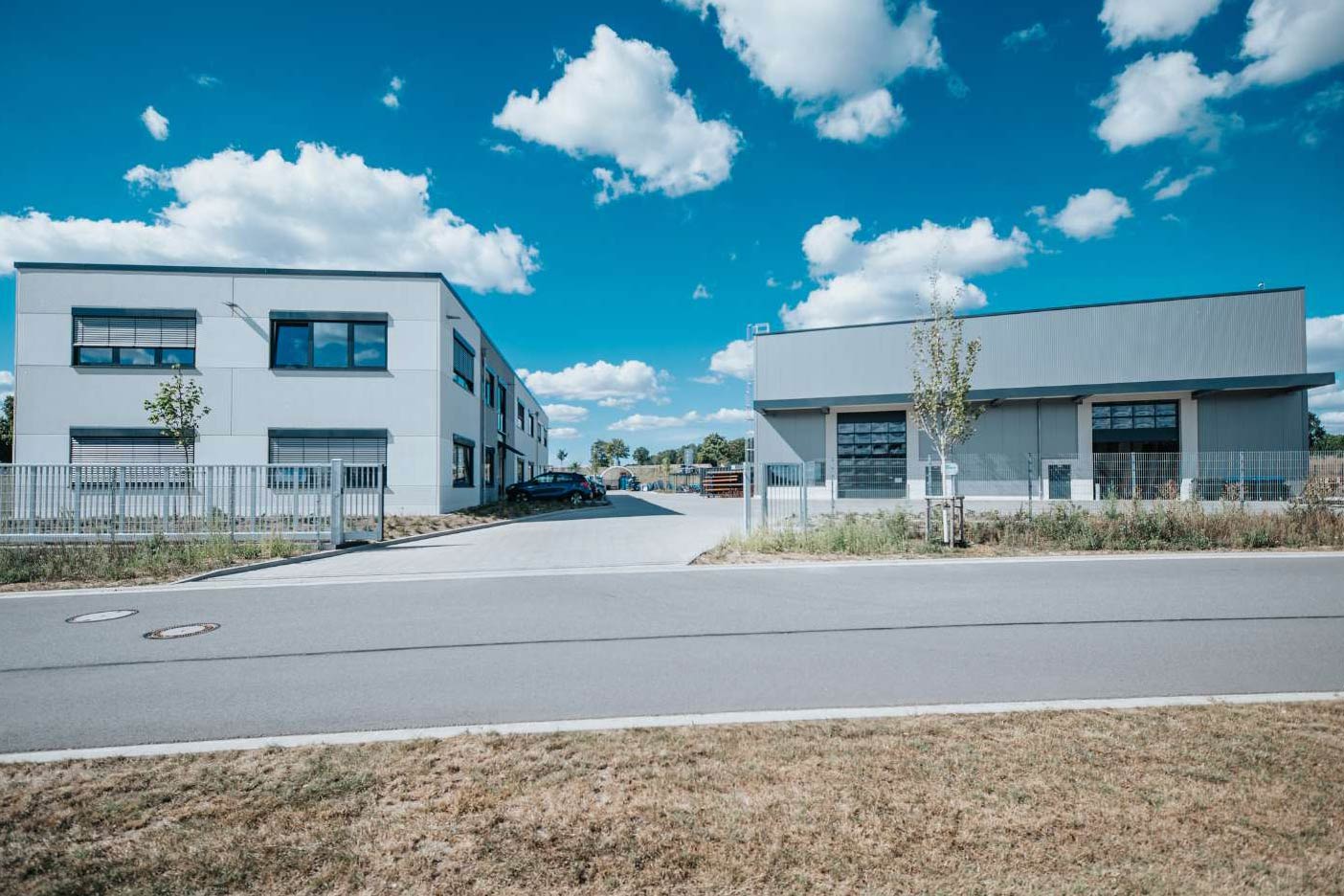 Werkhalle und Büro eines Maschinenbau-Unternehmens mit Zaun und geparktem Auto im Vordergrund.