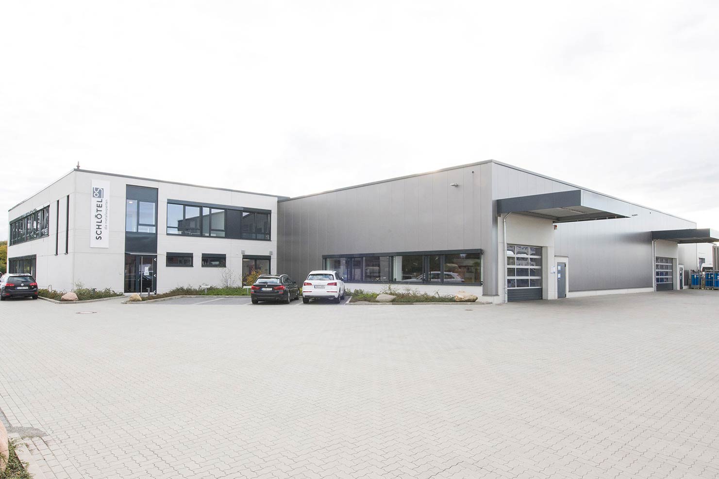 Moderne Produktionshalle mit Verwaltungsbereich für Metall-Handwerksbetrieb, Autos parken vor dem großen Industriegebäude.
