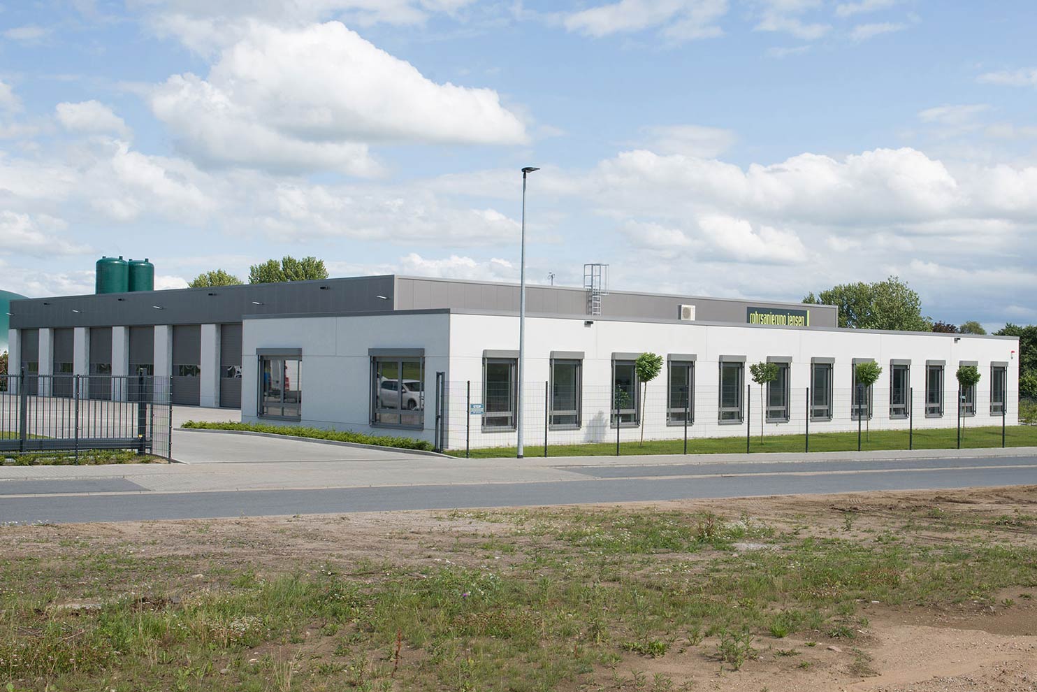 Neubau eines weißen Betriebsgebäudes mit Fahrzeughalle, eingebettet in eine grüne Wiese für ein Handwerksunternehmen.