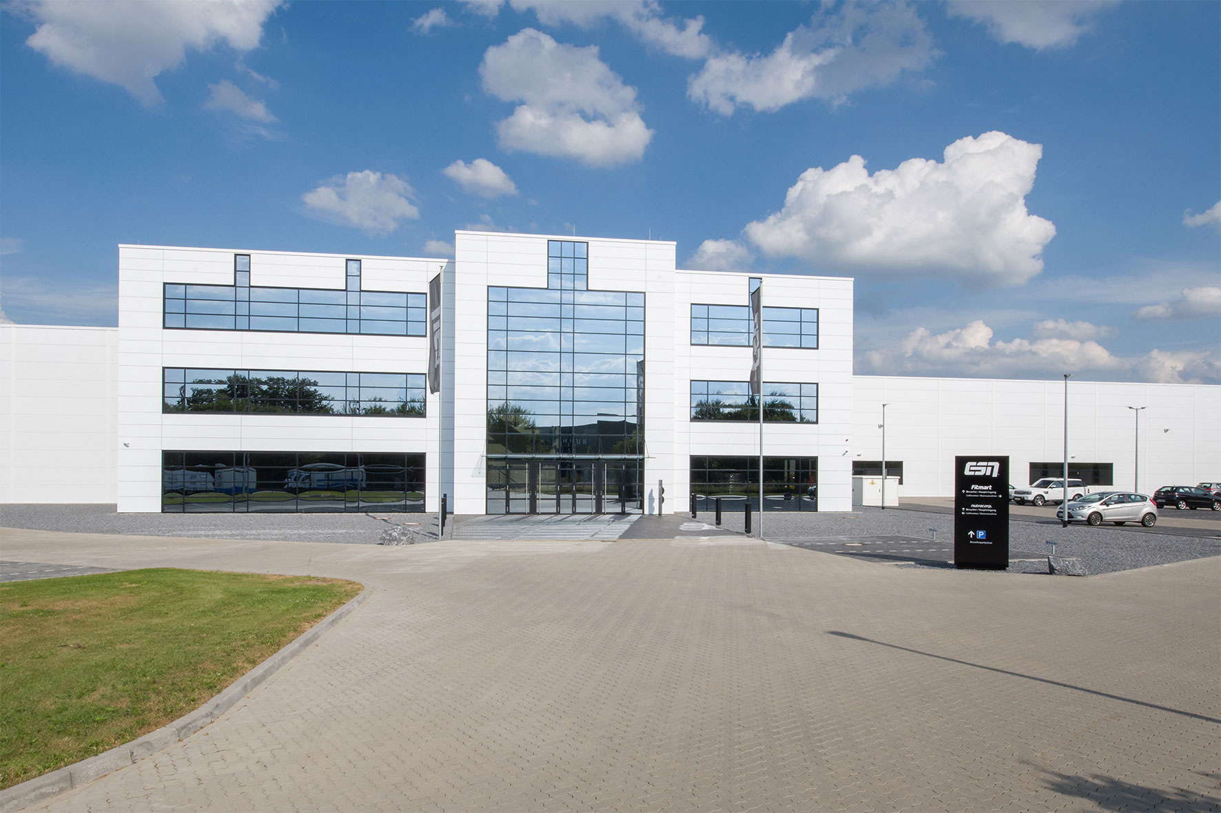 Weißes Gebäude mit Parkplatz, genutzt für Produktion und Verwaltung im Großhandel von Nahrungsergänzungsmitteln.