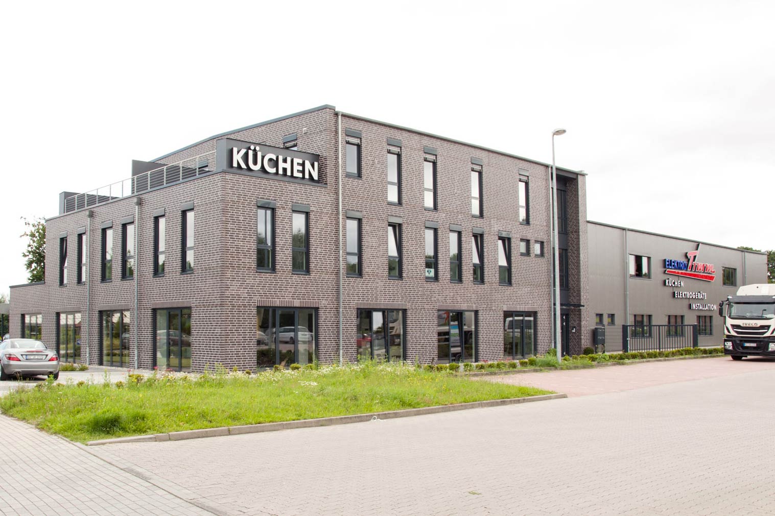 Großes Firmenschild an einem großen Betriebsgebäude eines Elektrofachbetriebs mit Küchenausstellung.