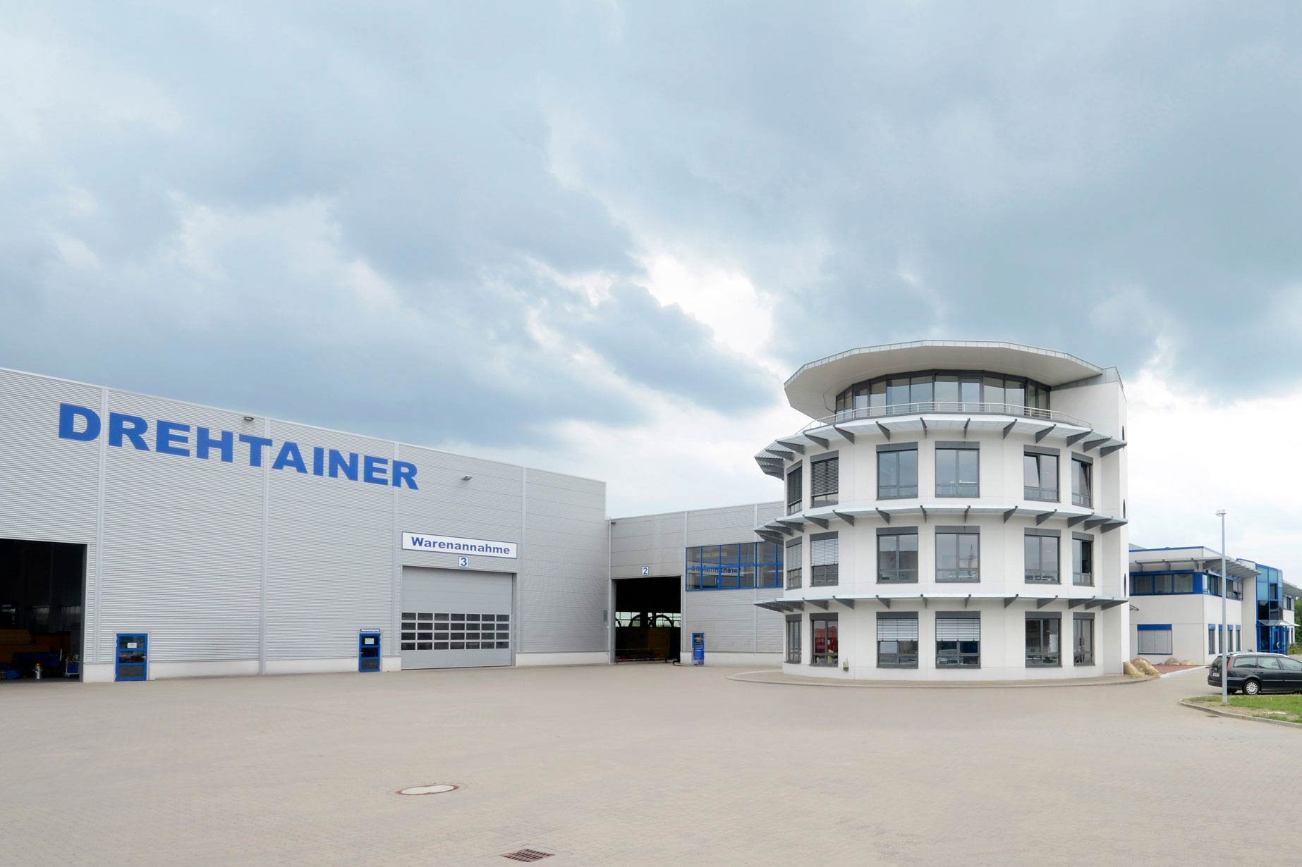 Betriebsgebäude für metallverarbeitenden Betrieb mit Penthouse, vor dem mehrere Autos abgestellt sind.